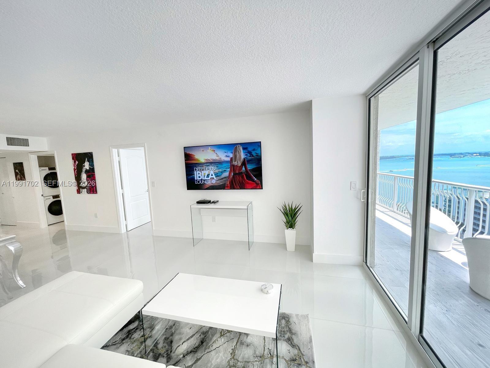 A bright living room features white tile floors, a wall-mounted television, and a balcony view — 1200 SE Brickell Bay Dr # 1707, Miami FL 33131, MIAMI, FL