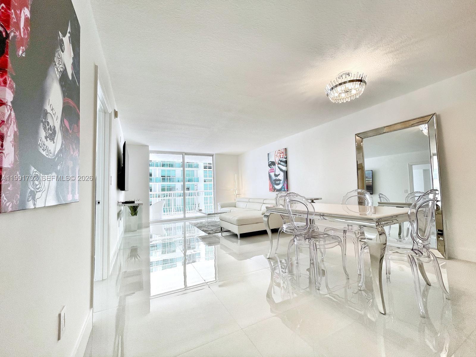 A bright, open-concept living and dining area features white tile floors and modern transparent chairs — 1200 SE Brickell Bay Dr # 1707, Miami FL 33131, MIAMI, FL
