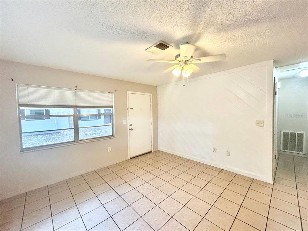 An empty room features light-colored tile flooring, a ceiling fan, and a white front door — 5800 MONTANA AVENUE, NEW PORT RICHEY, FL