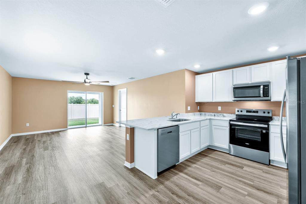 An open-concept living area features light brown walls, wood-look flooring, and a view into the kitchen — 5029 ROCKY COAST PLACE, PALMETTO, FL