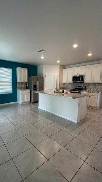 A kitchen with white cabinets, a granite island, stainless steel appliances, and light tile flooring — 494 JACKS WAY, DAVENPORT, FL