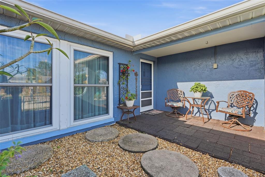 A blue house exterior features a paved patio, two chairs, a table, and stepping stones — 3226 FAIRMOUNT DRIVE, HOLIDAY, FL