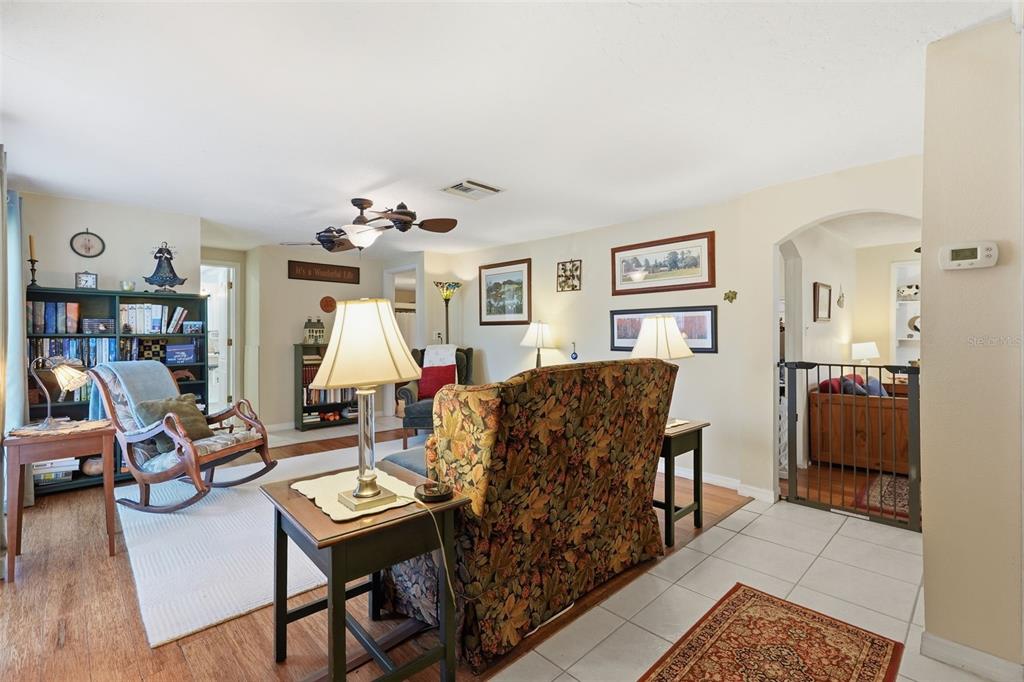 A living room features a floral sofa, a rocking chair, bookshelves, and tile and wood flooring — 3226 FAIRMOUNT DRIVE, HOLIDAY, FL