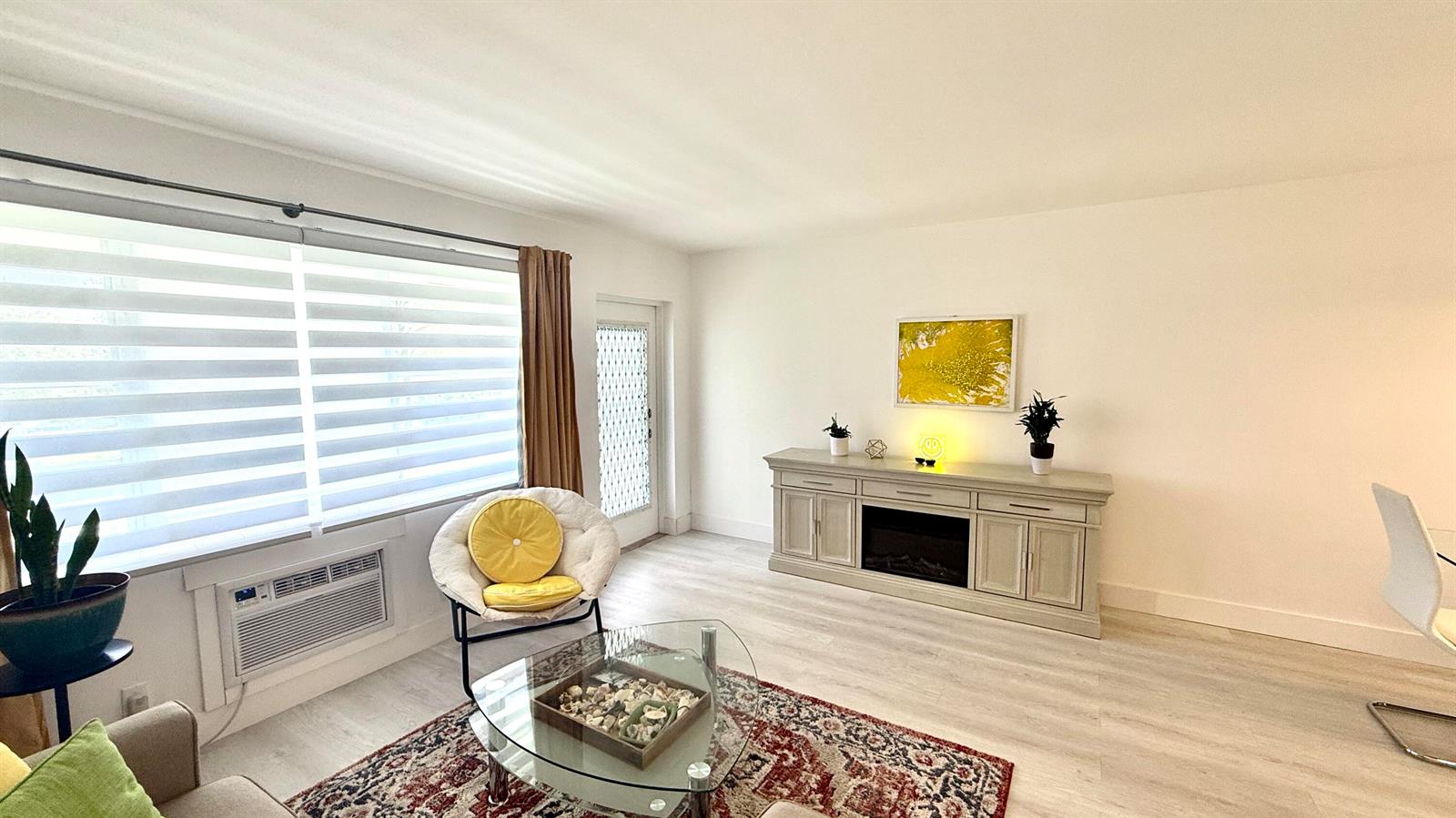 A living room features light wood flooring, a fireplace console, a glass coffee table, and windows — 78 Harwood H Crescent, Deerfield Beach FL 33442, DEERFIELD BEACH, FL