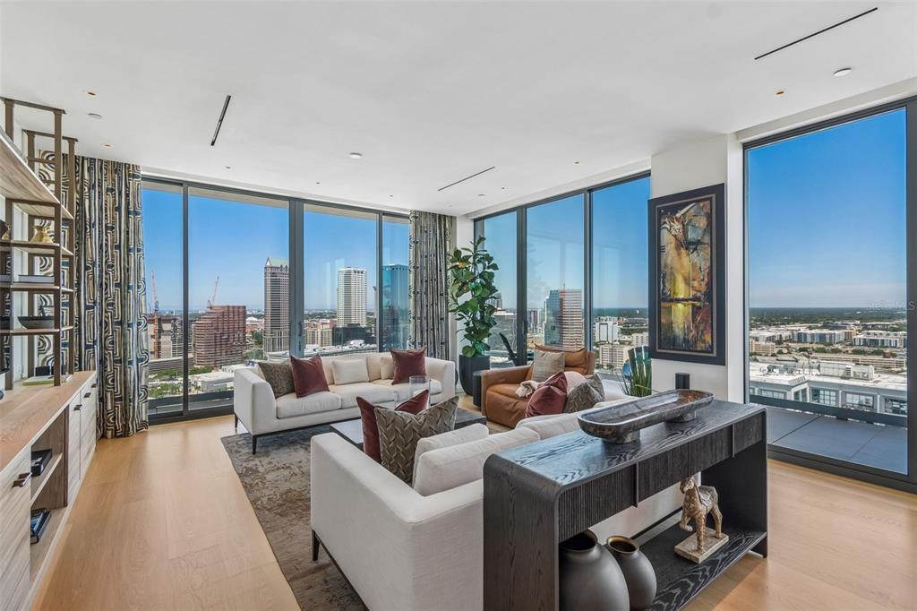 A modern living room features floor-to-ceiling windows with city views, neutral furniture, and wood flooring — 1000 WATER STREET UNIT 2501, TAMPA, FL