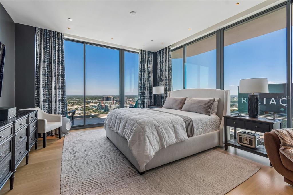 A modern bedroom features a large bed, floor-to-ceiling windows, and panoramic city views — 1000 WATER STREET UNIT 2501, TAMPA, FL