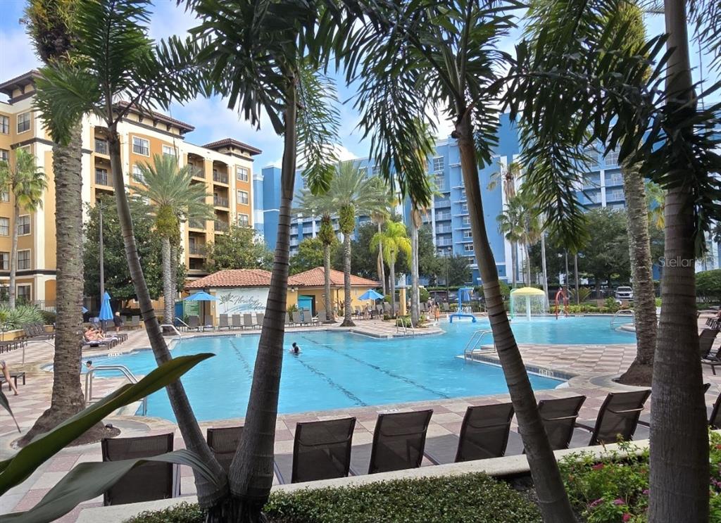 A swimming pool with lounge chairs and palm trees sits between two large apartment buildings — 12556 FLORIDAYS RESORT DRIVE UNIT A-201, ORLANDO, FL