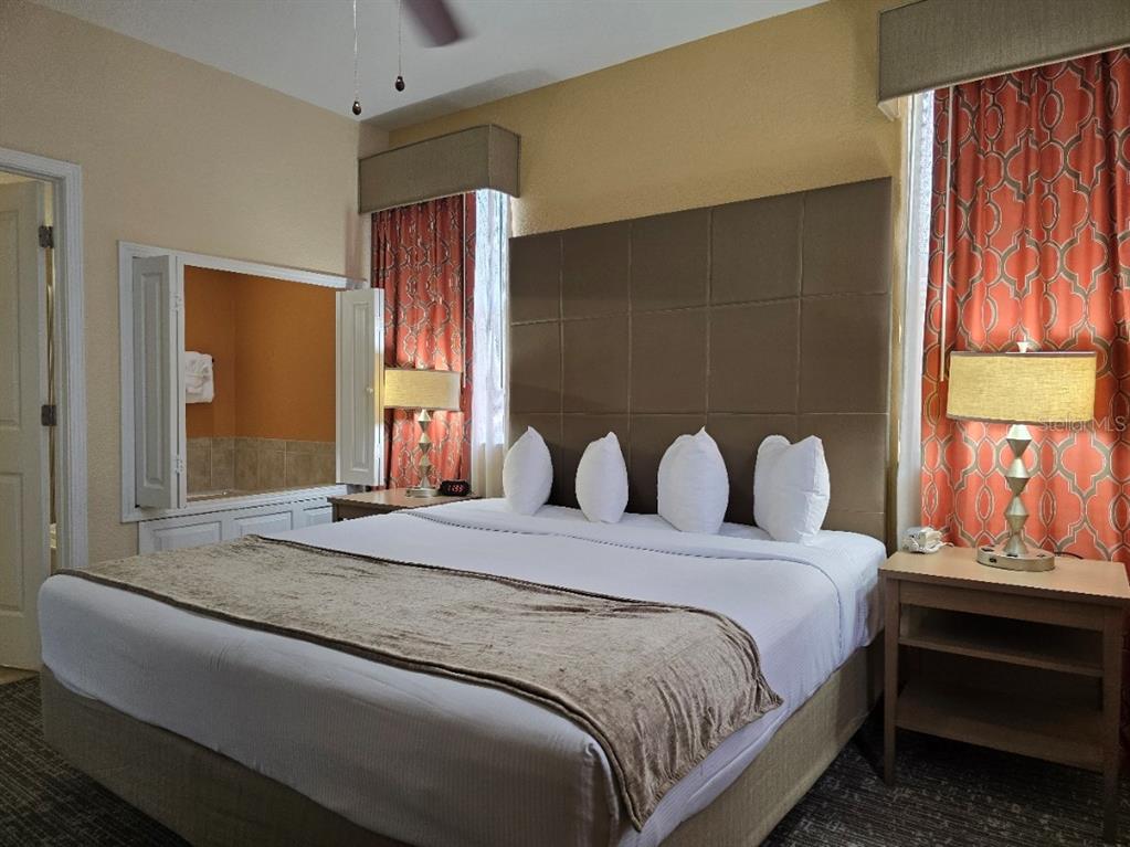 A hotel bedroom features a king bed with a tall headboard and orange patterned curtains — 12556 FLORIDAYS RESORT DRIVE UNIT A-201, ORLANDO, FL