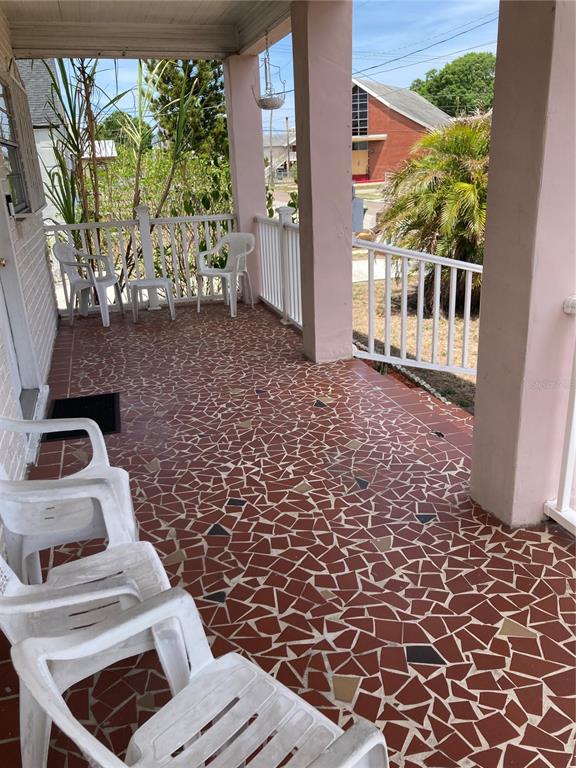 A covered porch features a red mosaic tile floor, white railings, and several plastic chairs — 2405 CORRINE STREET, TAMPA, FL