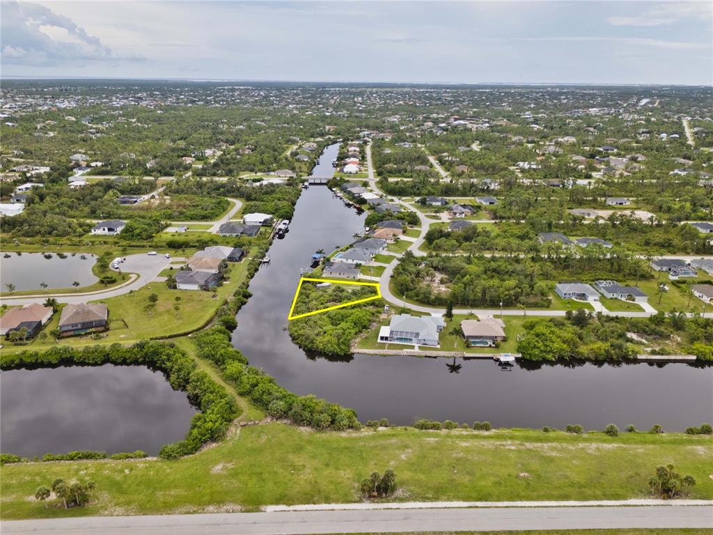 An aerial view shows a vacant, triangular waterfront lot outlined in yellow along a canal — 8050 SANTA CRUZ DRIVE, PORT CHARLOTTE, FL
