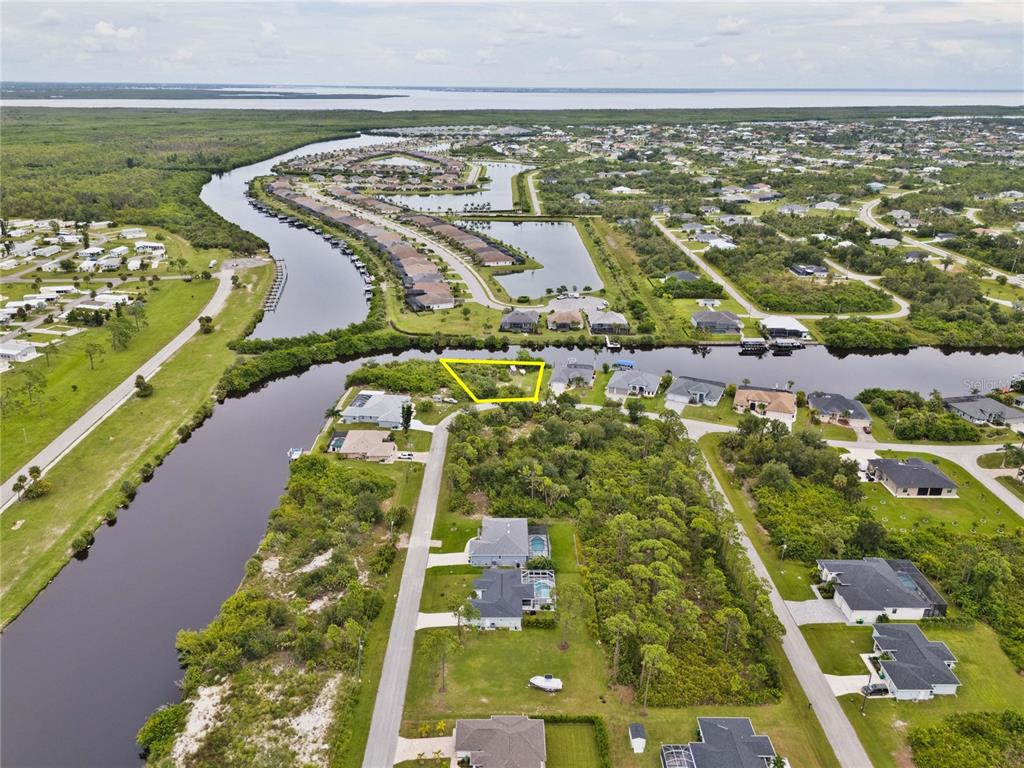 An aerial view shows a vacant, yellow-outlined waterfront lot in a residential neighborhood — 8050 SANTA CRUZ DRIVE, PORT CHARLOTTE, FL