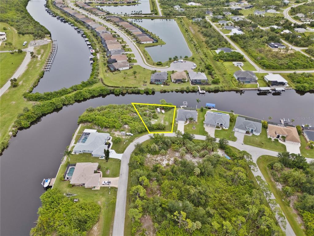 An aerial view shows a vacant waterfront lot outlined in yellow within a residential neighborhood — 8050 SANTA CRUZ DRIVE, PORT CHARLOTTE, FL