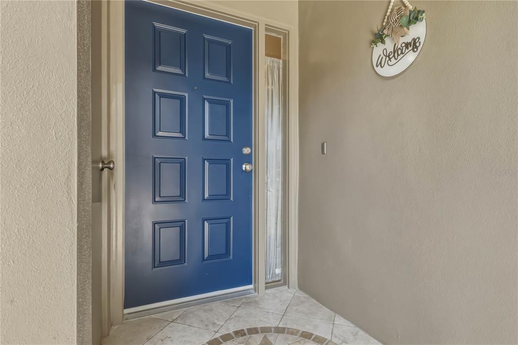 A blue front door with eight rectangular panels sits next to a vertical glass sidelight — 1696 NASH COURT, DUNEDIN, FL