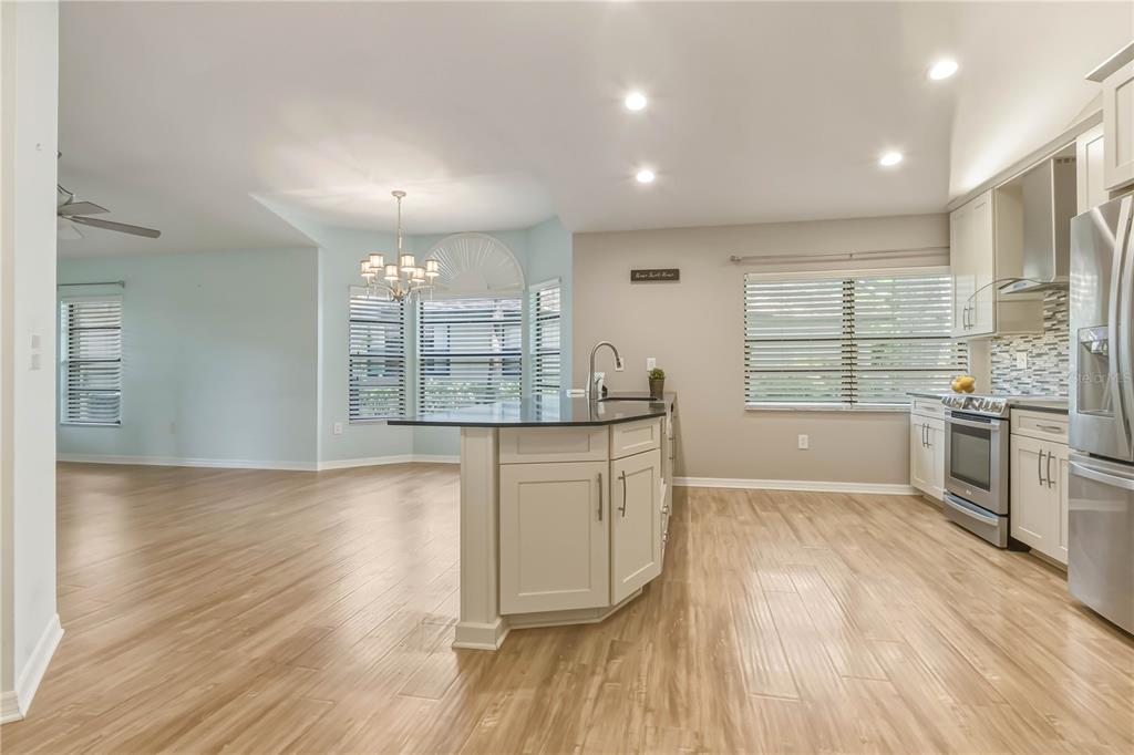 A kitchen with light-colored cabinets, a dark island countertop, and light wood-look flooring — 1696 NASH COURT, DUNEDIN, FL