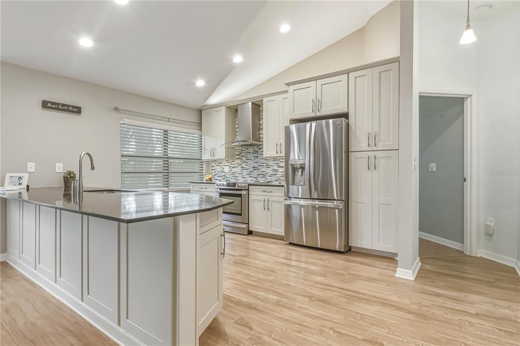 A modern kitchen features light gray cabinets, stainless steel appliances, and a dark granite island — 1696 NASH COURT, DUNEDIN, FL