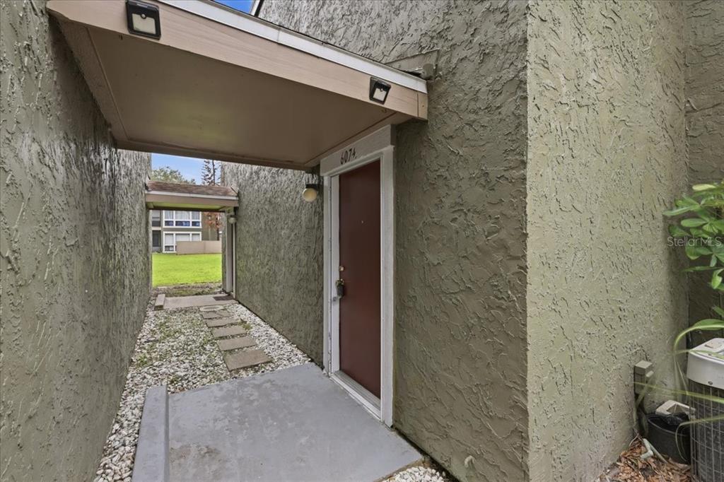 A brown front door is set into a stucco exterior wall beneath a covered entryway — 6074 PEREGRINE AVENUE UNIT B02, ORLANDO, FL
