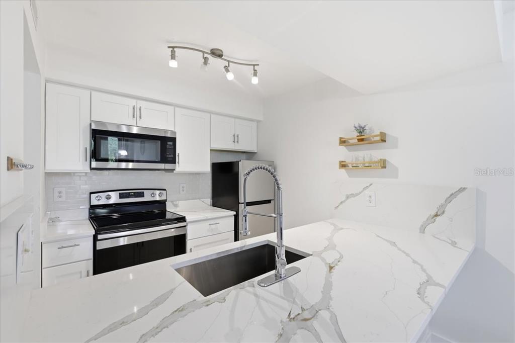 A modern kitchen features white cabinets, stainless steel appliances, and a marble-patterned quartz countertop — 6074 PEREGRINE AVENUE UNIT B02, ORLANDO, FL