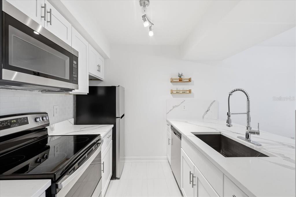 A modern kitchen features white cabinets, marble-look countertops, stainless steel appliances, and a farmhouse sink — 6074 PEREGRINE AVENUE UNIT B02, ORLANDO, FL