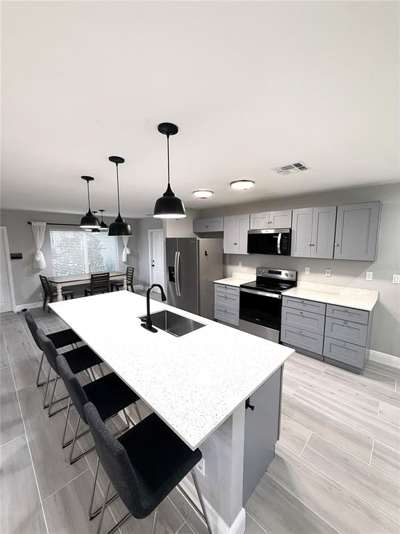 A modern kitchen features a large white quartz island, gray cabinetry, and stainless steel appliances — 12480 SW 2ND STREET, PLANTATION, FL