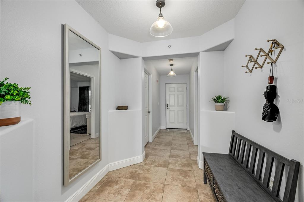 An entryway features tile flooring, a large wall mirror, a bench, and a front door — 551 CASA BELLA DRIVE UNIT 206, CAPE CANAVERAL, FL