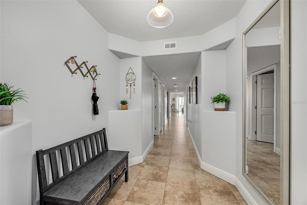 A hallway features tile flooring, a wooden bench, a large mirror, and recessed lighting — 551 CASA BELLA DRIVE UNIT 206, CAPE CANAVERAL, FL