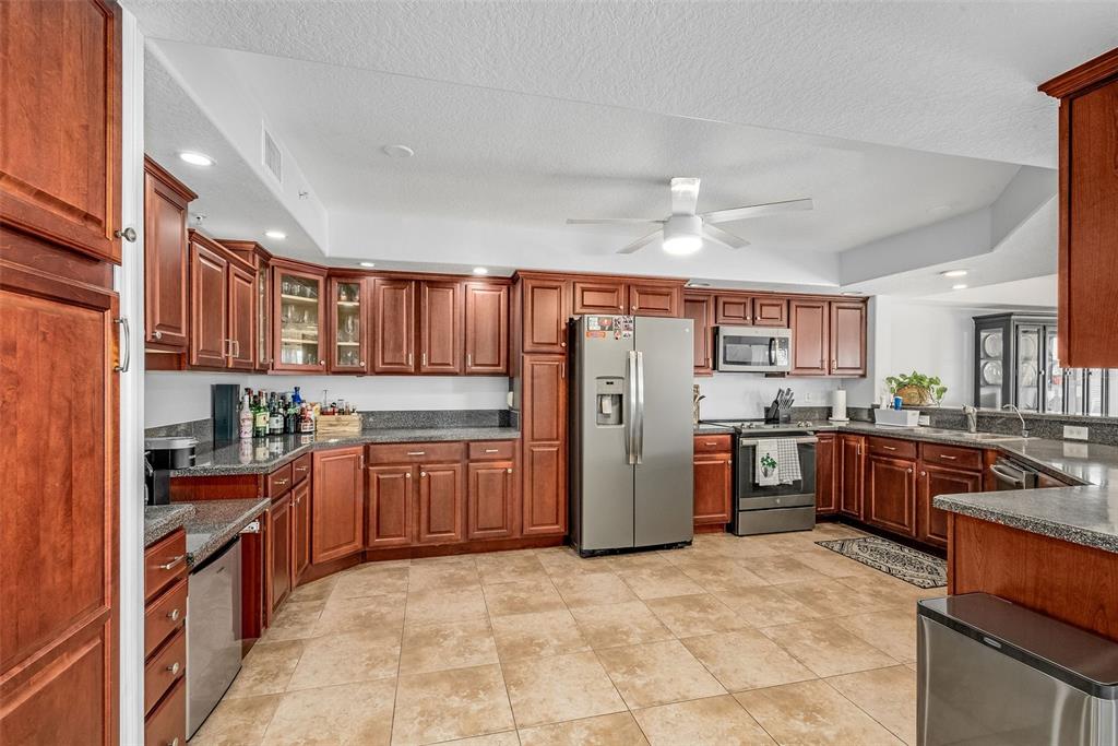 A kitchen features cherry wood cabinets, granite countertops, stainless steel appliances, and beige tile flooring — 551 CASA BELLA DRIVE UNIT 206, CAPE CANAVERAL, FL