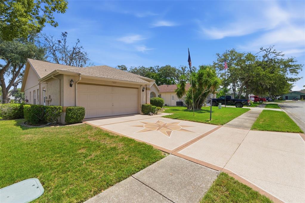 A single-story house with a two-car garage and a decorative compass rose on the driveway — 9851 KINGSPORT AVENUE, NEW PORT RICHEY, FL