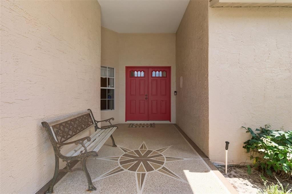 A covered entryway features a red double door, a decorative compass rose floor, and bench — 9851 KINGSPORT AVENUE, NEW PORT RICHEY, FL
