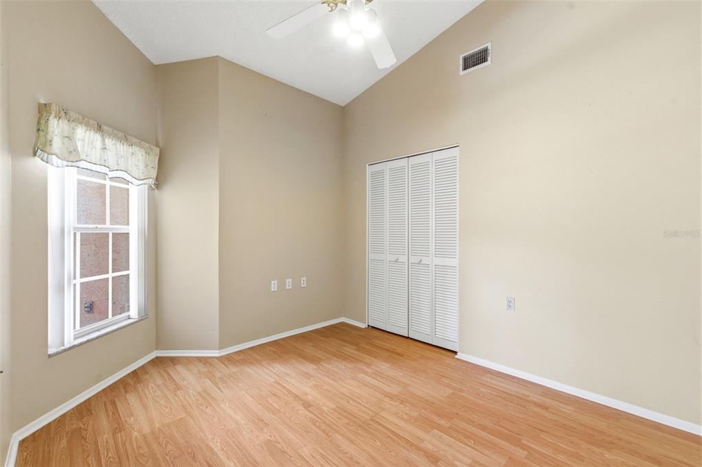 An empty bedroom features light-colored walls, wood-look flooring, a ceiling fan, and a white closet — 9851 KINGSPORT AVENUE, NEW PORT RICHEY, FL
