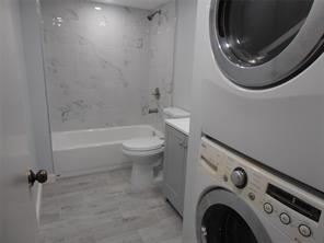 A bathroom with a bathtub, toilet, vanity, and a stacked washer and dryer unit — LAUDERHILL, FL