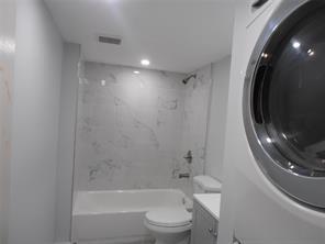 A bathroom features a white bathtub with marble-style tile walls and a stacked laundry unit — LAUDERHILL, FL