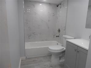 A bathroom featuring a white bathtub with marble-style tile walls, a toilet, and a gray vanity — LAUDERHILL, FL