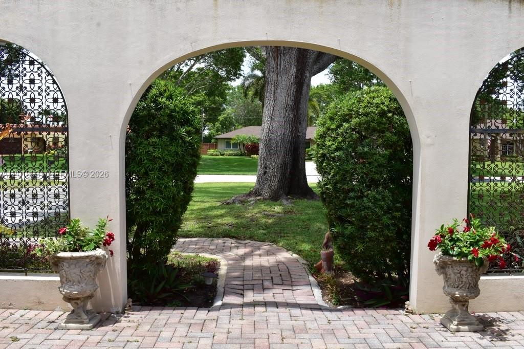 A brick path leads through a stucco archway flanked by potted plants and metal grilles — 3634 Lowson Blvd, Delray Beach FL 33445, DELRAY BEACH, FL