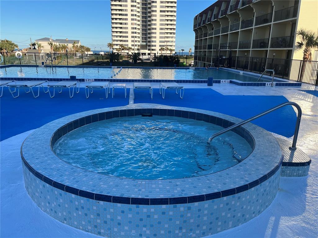 A circular tiled hot tub sits on a pool deck in front of a swimming pool — 1433 N ATLANTIC AVENUE UNIT 223, DAYTONA BEACH, FL
