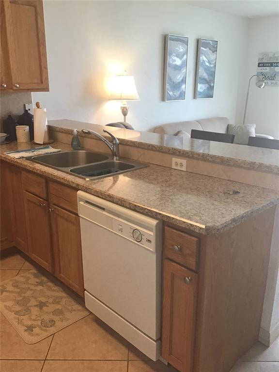 A kitchen features wood cabinets, granite countertops, a stainless steel sink, and a white dishwasher — 1433 N ATLANTIC AVENUE UNIT 223, DAYTONA BEACH, FL