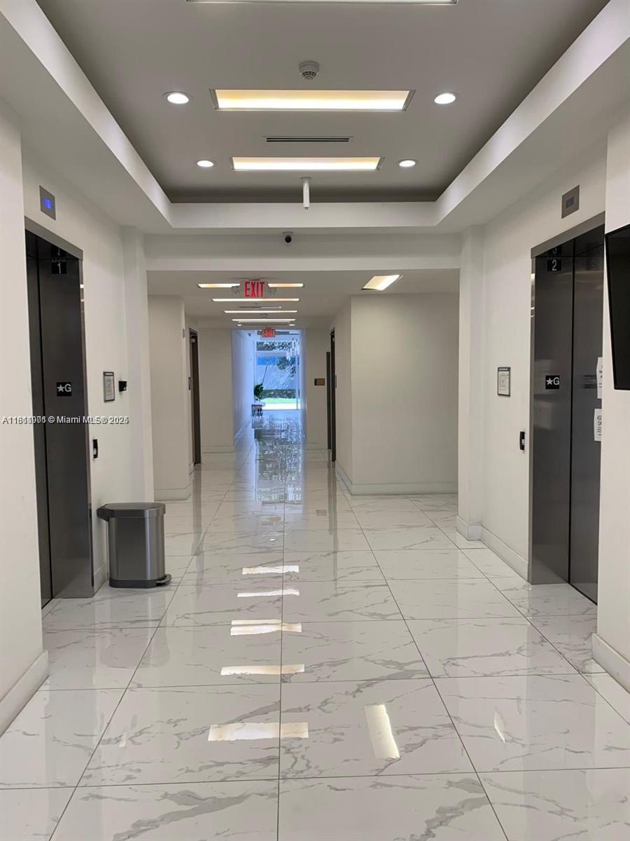 A bright hallway features white marble-look tile floors, two elevators, and a distant exit door — 10450 NW 33rd St # 309, Doral FL 33172, DORAL, FL