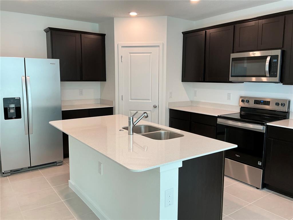 A kitchen features dark cabinets, stainless steel appliances, a white island, and light countertops — 3772 BENHAM RISE ROAD, SPRING HILL, FL