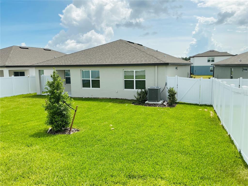 The backyard of a single-story house features a green lawn, white vinyl fencing, and an AC unit — 3772 BENHAM RISE ROAD, SPRING HILL, FL
