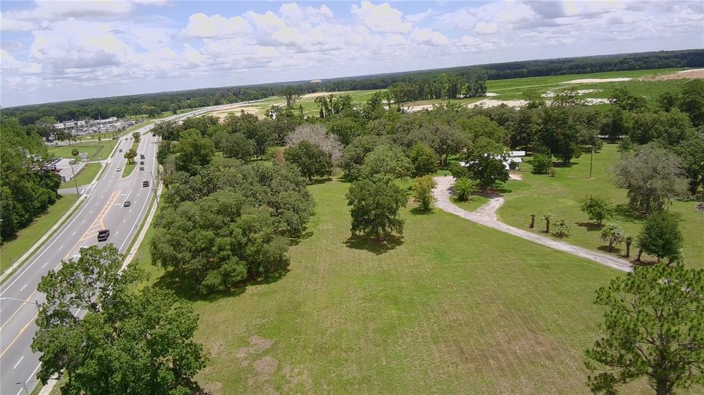 An aerial view shows a large grassy lot with scattered trees next to a paved road — 24206 DOC KARELAS DRIVE, NEWBERRY, FL