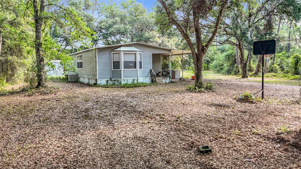 A single-story manufactured home sits on a large, leaf-covered lot with a basketball hoop — 38625 COUNTY LINE ROAD, ZEPHYRHILLS, FL