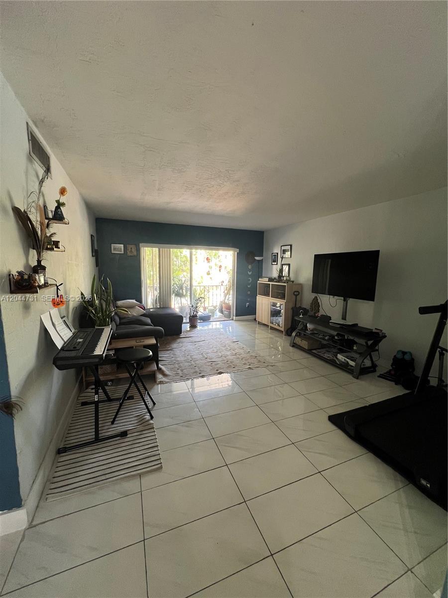 A living room features white tile flooring, a dark accent wall, and a sliding glass door — 6900 N Kendall Dr # A205, Pinecrest FL 33156, PINECREST, FL