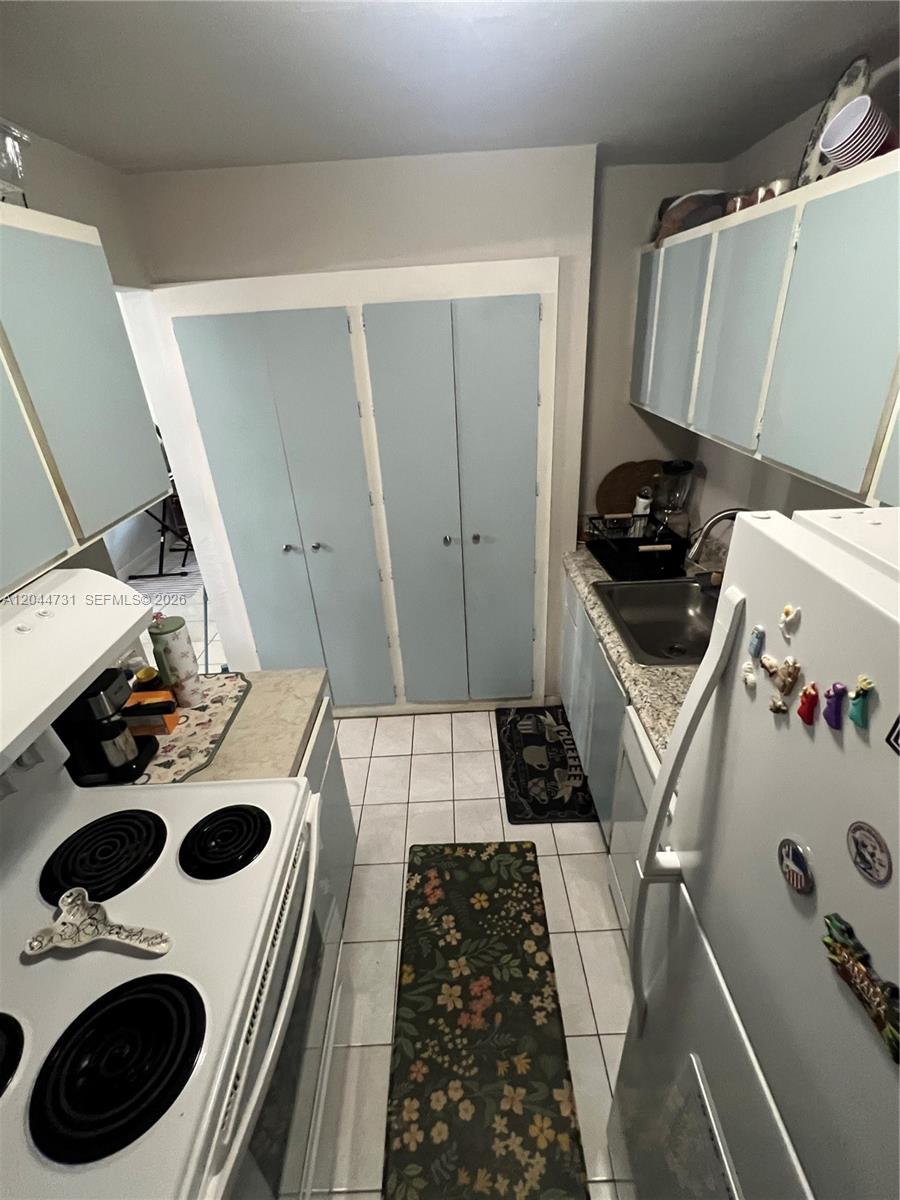 A galley kitchen features light blue cabinets, white appliances, and a floral runner rug — 6900 N Kendall Dr # A205, Pinecrest FL 33156, PINECREST, FL