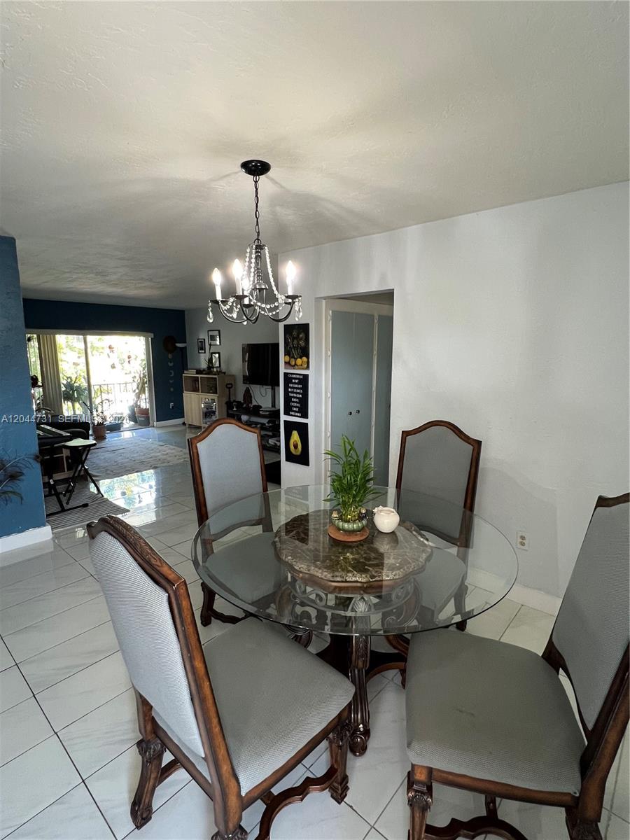A dining area features a glass-topped table with four upholstered chairs under a crystal chandelier — 6900 N Kendall Dr # A205, Pinecrest FL 33156, PINECREST, FL