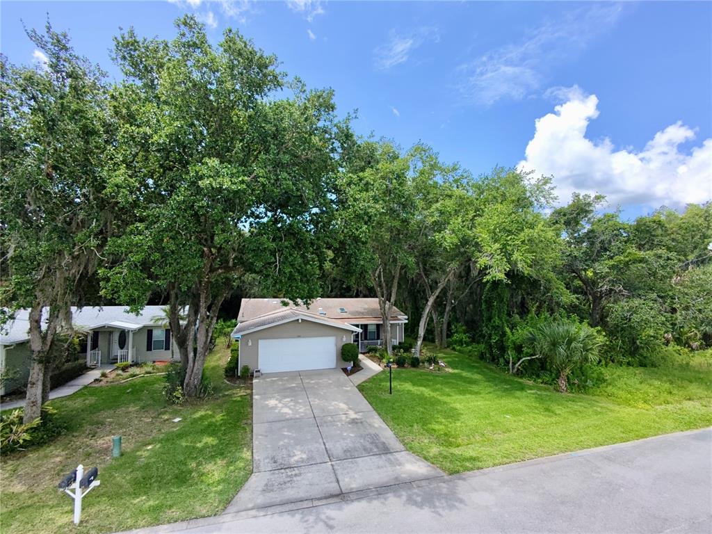 A single-story house with a white garage door and a concrete driveway sits among trees — 301 WATER LANDING DRIVE, OAK HILL, FL