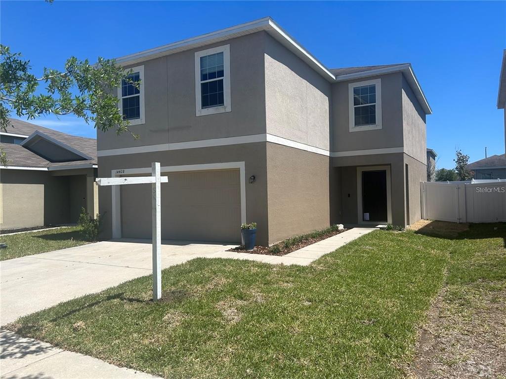 A two-story house with a beige stucco exterior, a two-car garage, and a front walkway — 14428 DUNROBIN DRIVE, WIMAUMA, FL