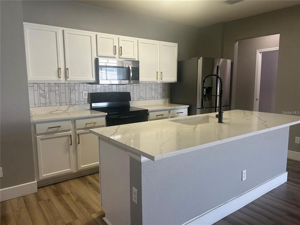 A kitchen features white cabinets, a marble-patterned island, stainless steel appliances, and gray walls — 14428 DUNROBIN DRIVE, WIMAUMA, FL