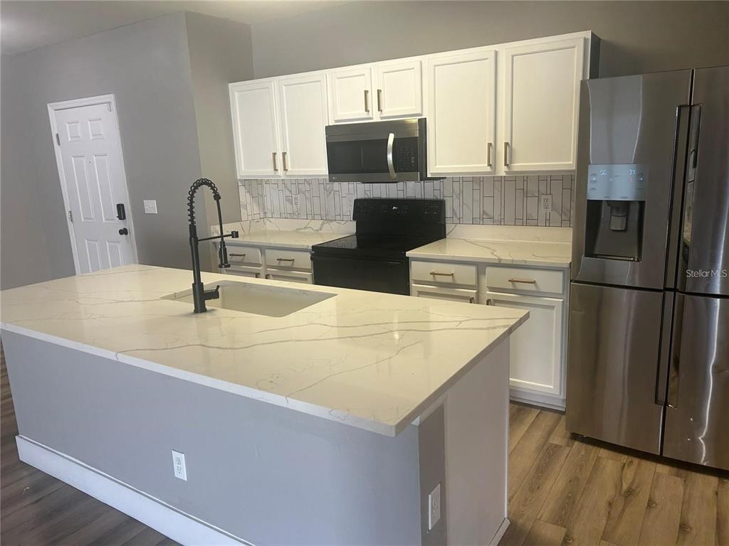 A kitchen features white cabinets, a marble-patterned island, stainless steel appliances, and wood-look flooring — 14428 DUNROBIN DRIVE, WIMAUMA, FL