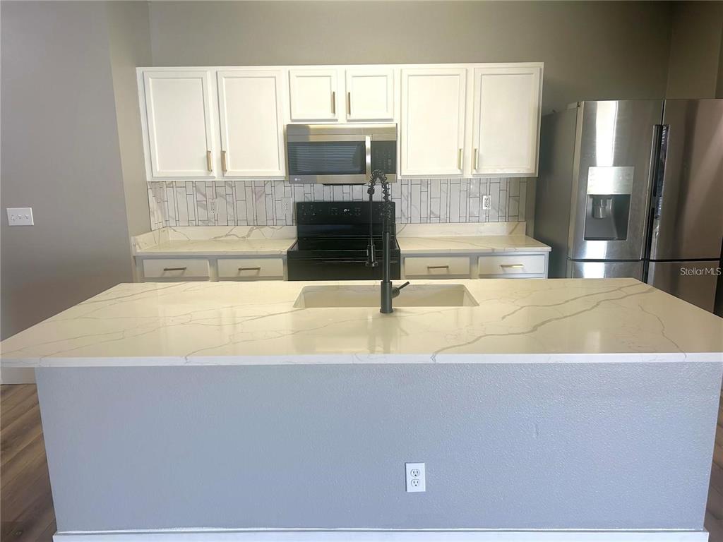 A kitchen features white cabinets, a quartz island with a sink, and stainless steel appliances — 14428 DUNROBIN DRIVE, WIMAUMA, FL