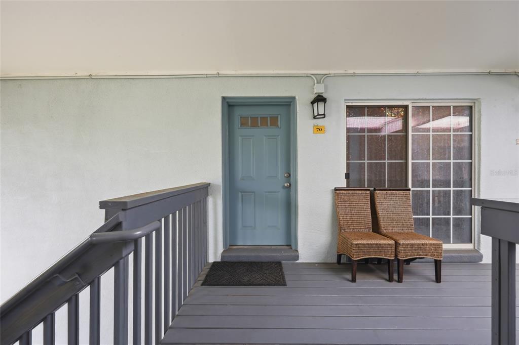 A blue front door and two wicker chairs sit on a gray wooden porch — 4888 CONWAY ROAD UNIT 70, ORLANDO, FL