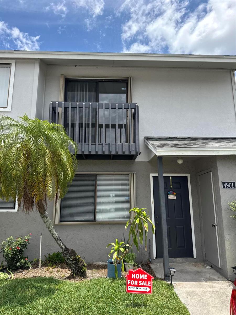 A two-story gray townhouse features a second-floor balcony, a dark front door, and a palm tree — 4901 Pier Drive, FL 33463, FL